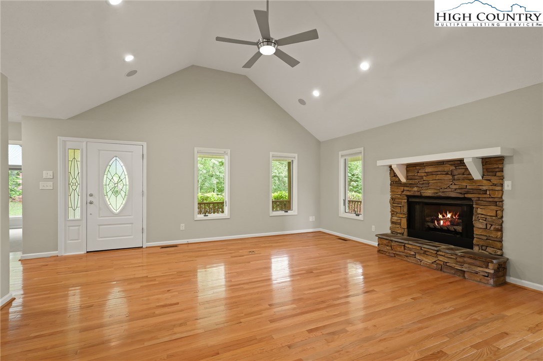 517 Willow Trail Boone, NC 28607 - Photo 5 of 26 an empty room with windows a fireplace a ceiling fan and wooden floor