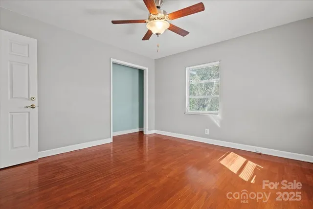 an empty room with wooden floor chandelier fan and windows