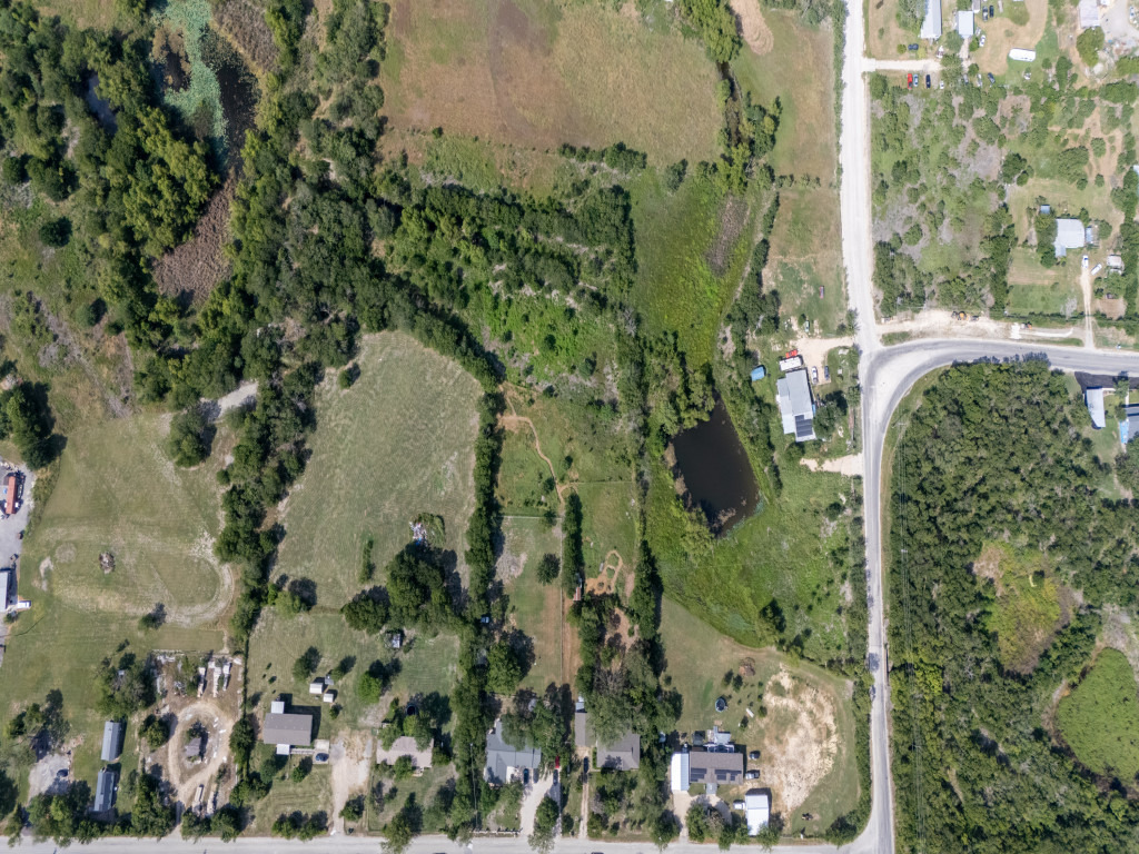 1035 Palomino Road Kyle, TX 78640 - Photo 9 of 13 Discover a sweeping aerial view revealing a verdant landscape with homes nestled among mature trees and open land.