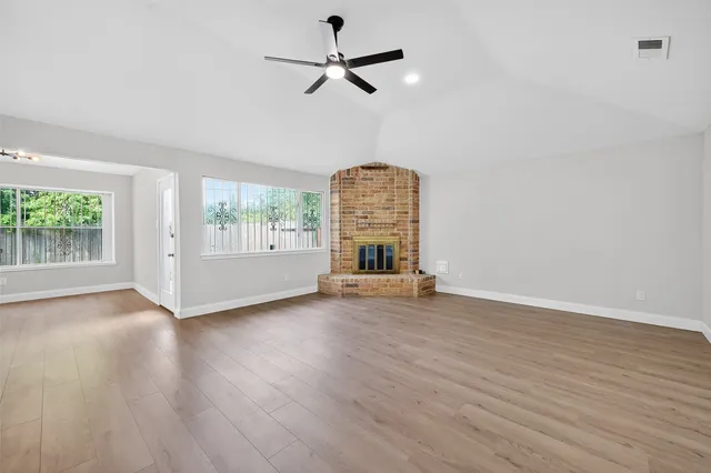 an empty room with wooden floor chandelier fan and windows