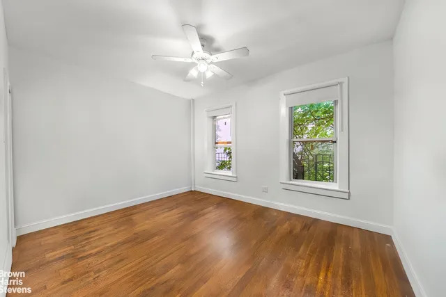 an empty room with a chandelier fan and wooden floor