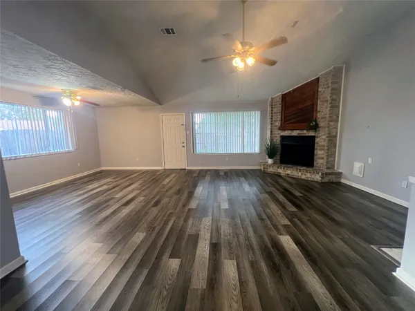 a view of an empty room with wooden floor and a kitchen