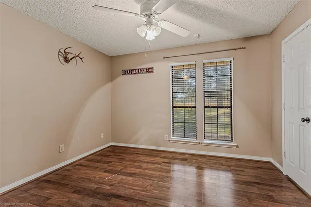 an empty room with wooden floor chandelier fan and windows