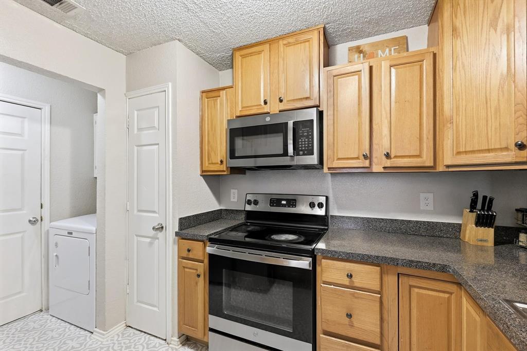 1312 Hackamore Street Mesquite, TX 75149 - Photo 9 of 23 Kitchen with stainless steel appliances, dark countertops, a textured ceiling, washer / dryer, and light wood finish cabinets