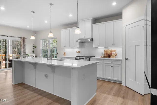 a kitchen with stainless steel appliances granite countertop a sink a stove a refrigerator and white cabinets with wooden floor