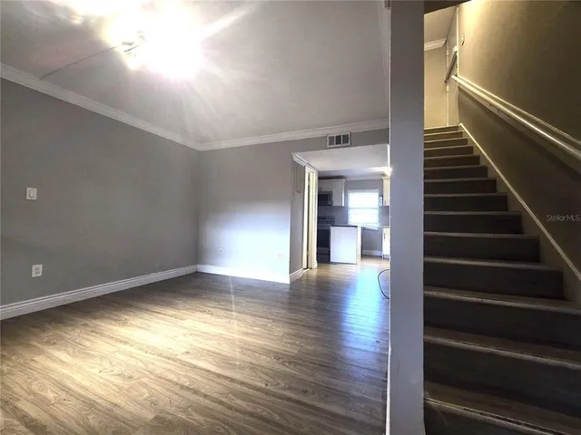 a view of an empty room with wooden floor and stairs