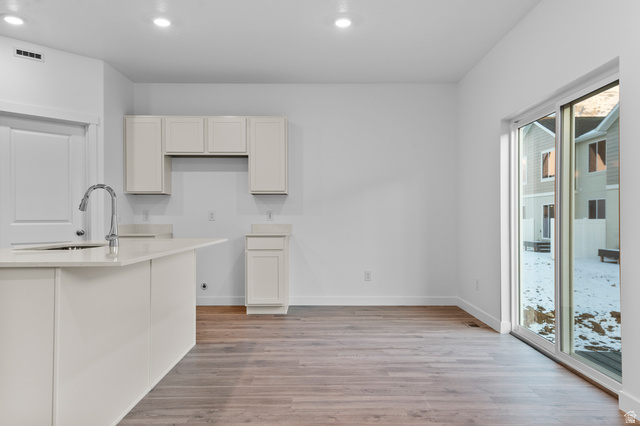 2829 North 710 West, Unit 15 Logan, UT 84321 - Photo 11 of 23 Open-concept kitchen and dining area featuring light wood-finish flooring, white walls, recessed lighting, a kitchen island with an integrated sink and gooseneck faucet, light-toned cabinetry, and sliding glass doors