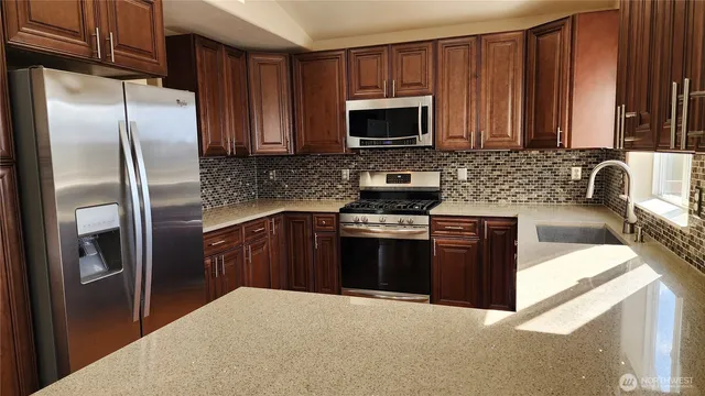 a kitchen with granite countertop a sink a stove top oven a refrigerator and dishwasher