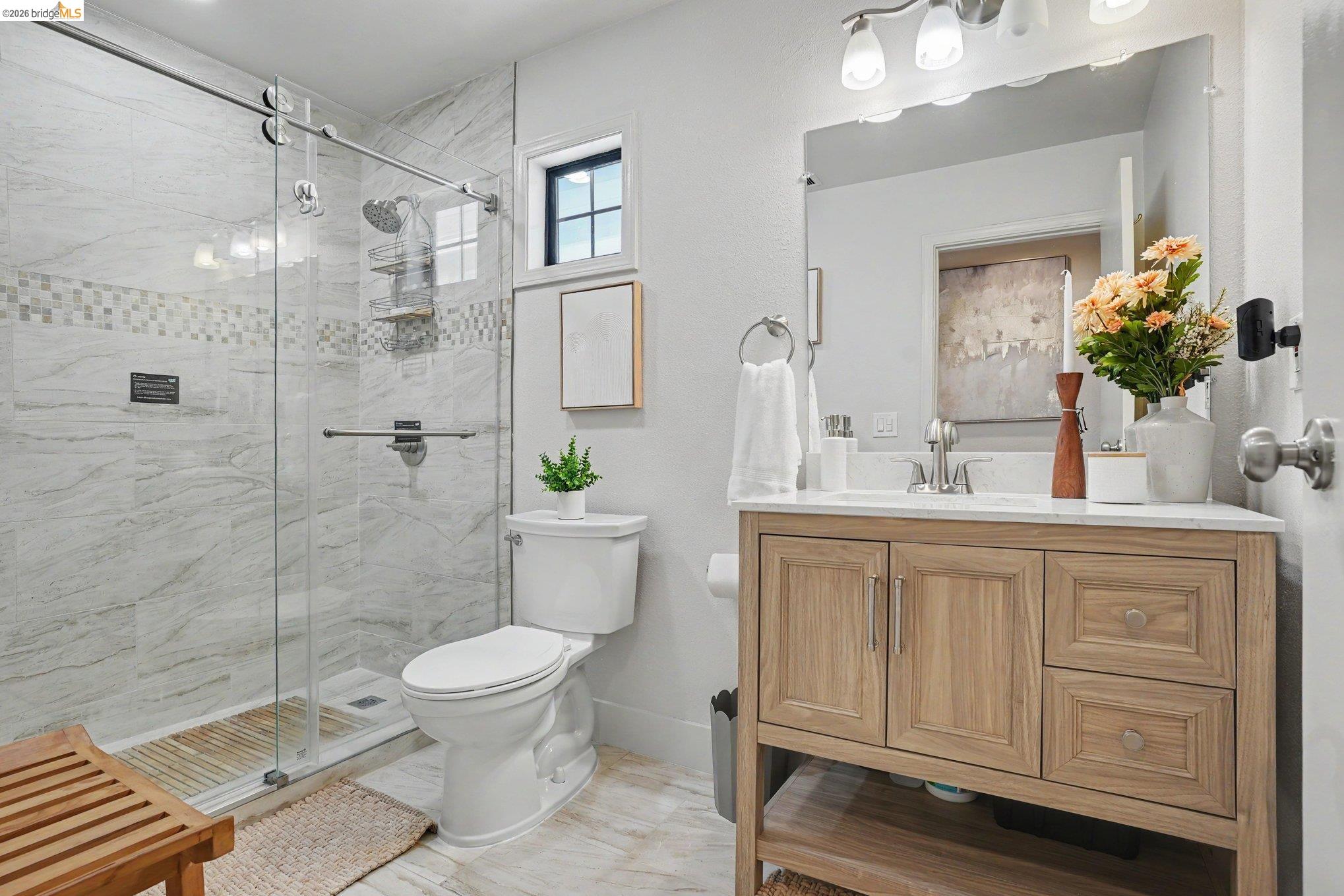 1433 Myrtle Street Oakland, CA 94607 - Photo 13 of 25 Renovated bathroom featuring a glass-enclosed shower with tile surround and mosaic accent, a wood-finish vanity with a white countertop and integrated sink, a contemporary mirror with overhead vanity lighting, and light-toned tile flooring
