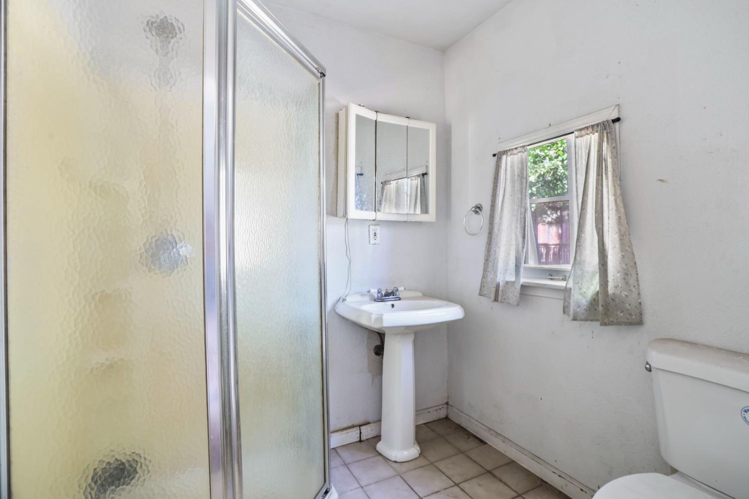 916 Elm Avenue Modesto, CA 95351 - Photo 47 of 52 ear dwelling bathroom with shower stall, pedestal sink, toilet, window, and tile flooring.