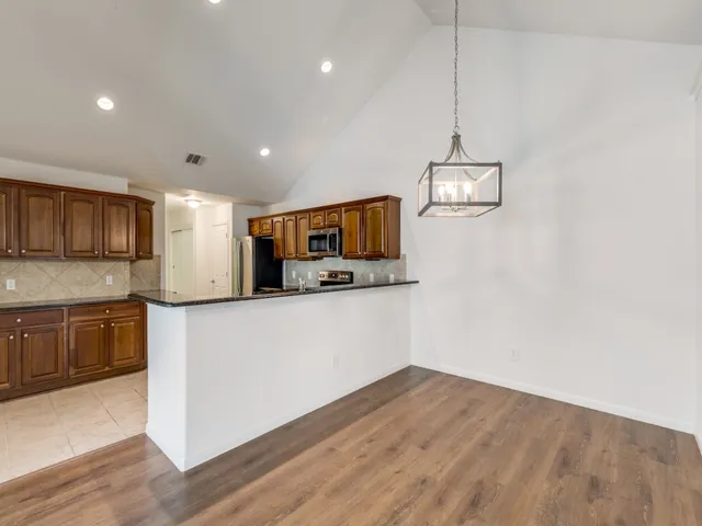 a kitchen with stainless steel appliances granite countertop a refrigerator a stove oven a sink dishwasher and white cabinets with wooden floor