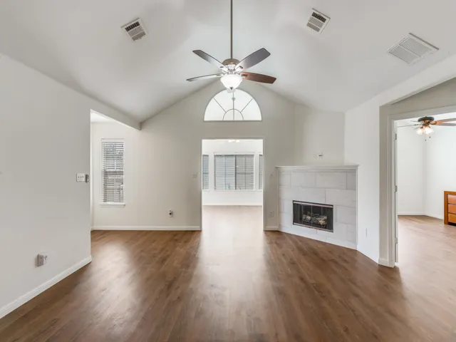 an empty room with wooden floor a chandelier fan and a fireplace