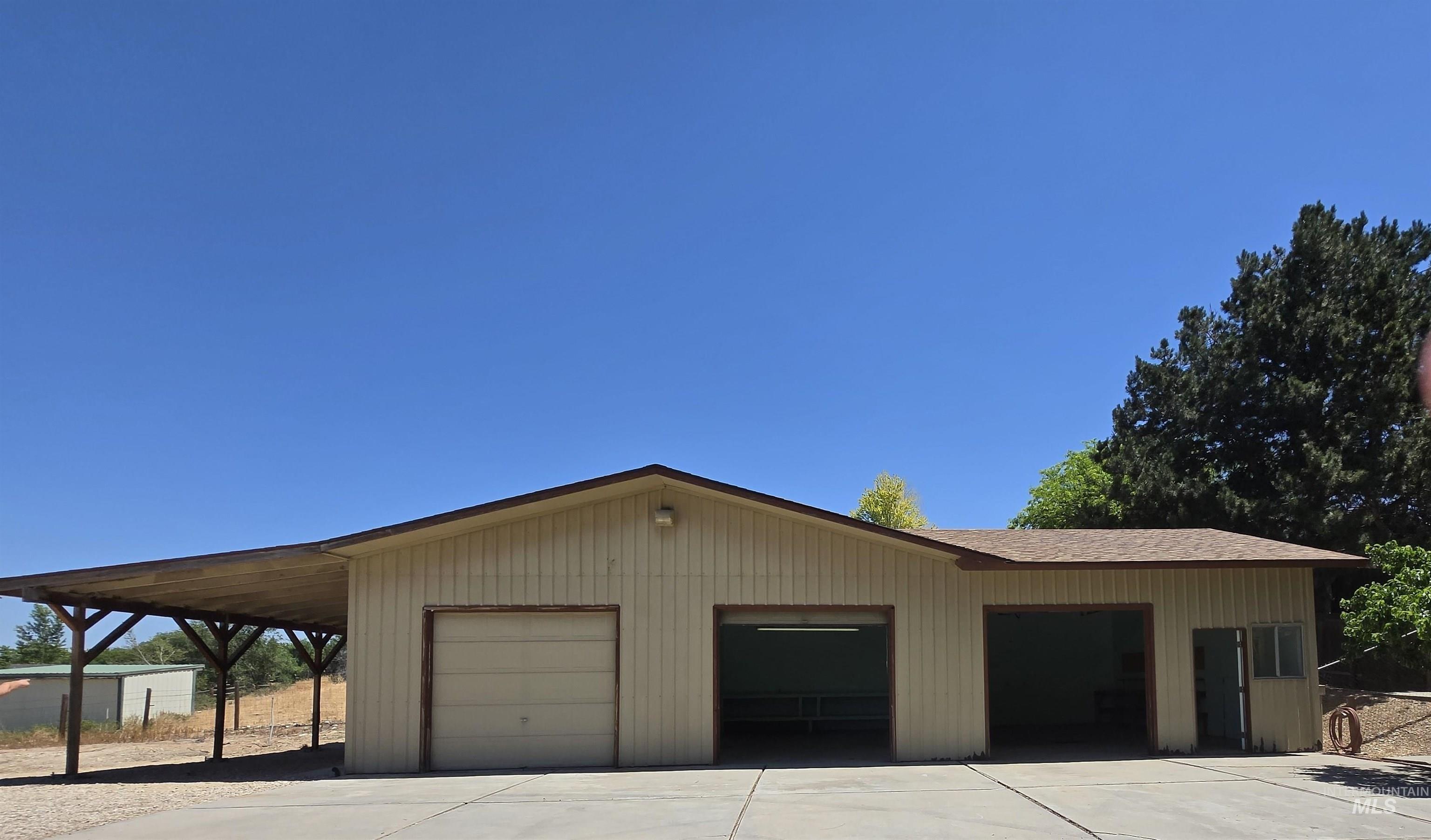 12050 West Hidden Valley Rim Road Boise, ID 83709 - Photo 24 of 39 Utility building featuring a two-bay garage with one roll-up door and one open bay, an additional open bay with an overhead light fixture, an exterior entry door, and a covered carport extension