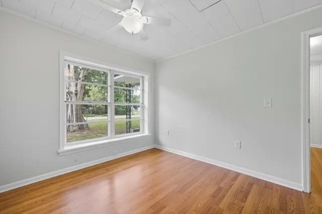 a view of an empty room with wooden floor and a ceiling fan