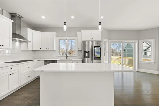 a large kitchen with stainless steel appliances granite countertop a refrigerator a sink dishwasher a oven and white cabinets with wooden floor