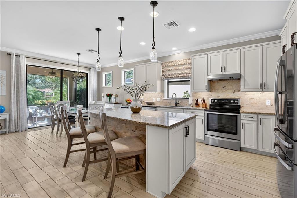 5215 Ciatto Way Ave Maria, FL 34142 - Photo 8 of 46 a kitchen with stainless steel appliances granite countertop a stove top oven a refrigerator a sink and a dining table with wooden floor