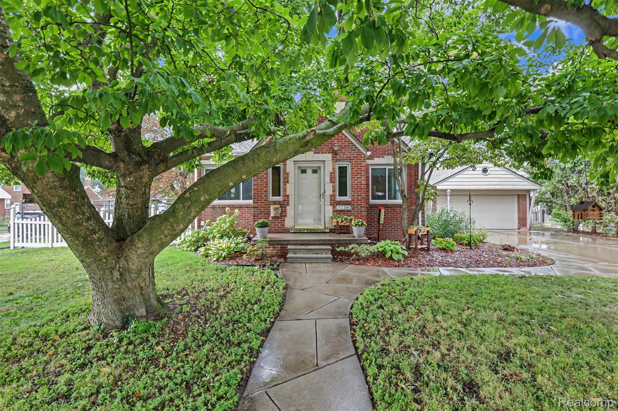 Brick exterior, white front door with sidelights, concrete pathway, attached garage, and mature landscaping