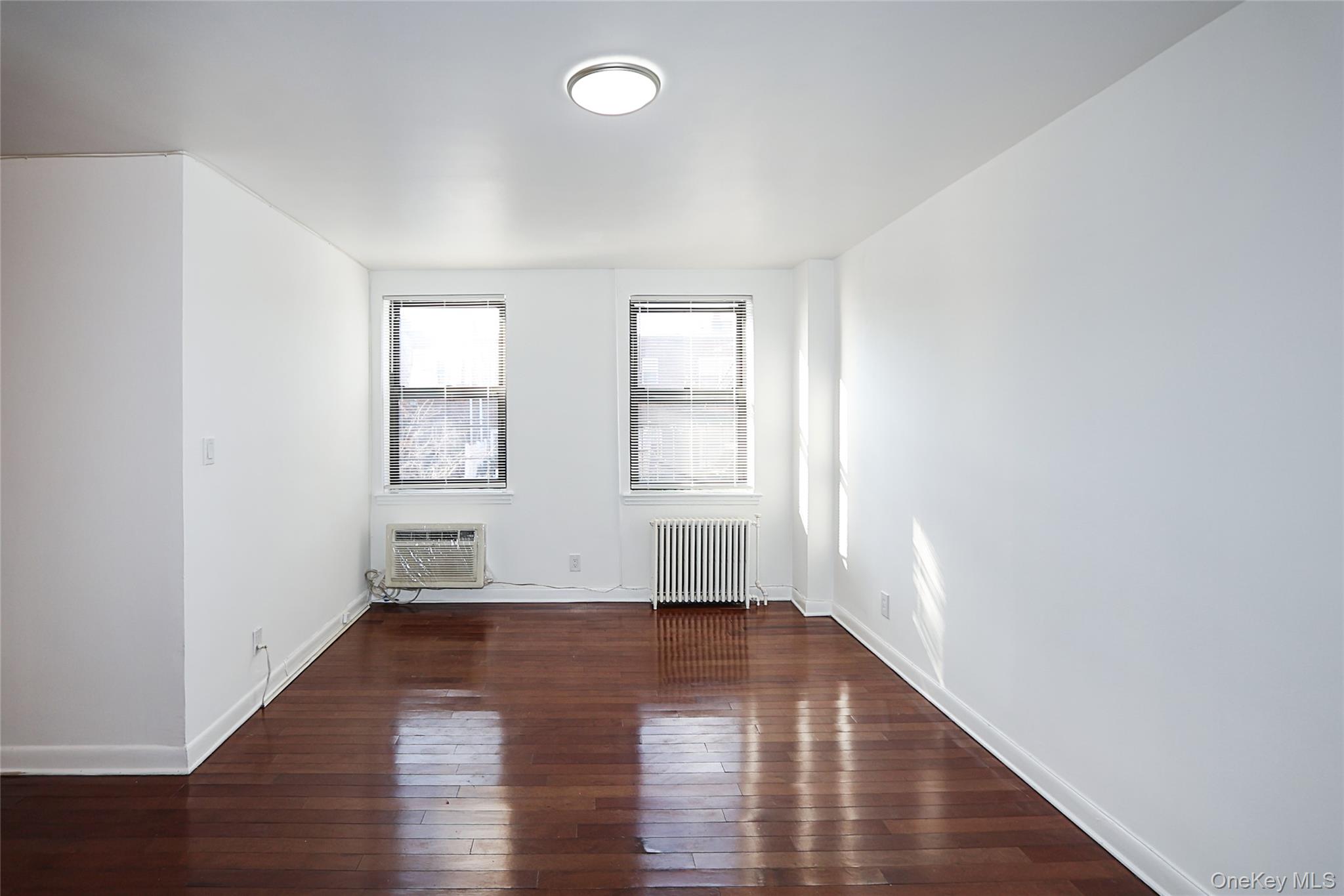 47-22 215th Place, Unit 2C Queens, NY 11361 - Photo 11 of 26 Unfurnished room with dark wood-style flooring, radiator heating unit, and a wall mounted AC