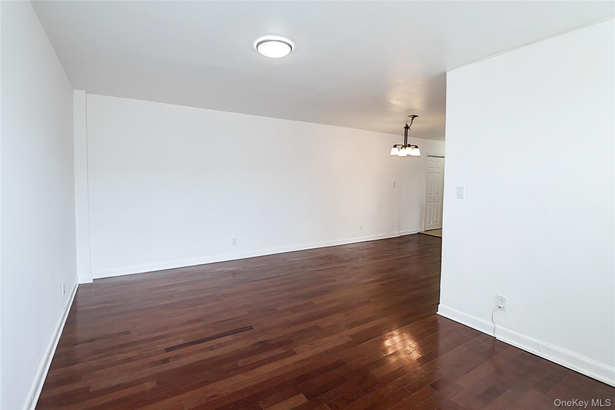 47-22 215th Place, Unit 2C Queens, NY 11361 - Photo 13 of 26 Unfurnished room with dark wood-type flooring and a chandelier
