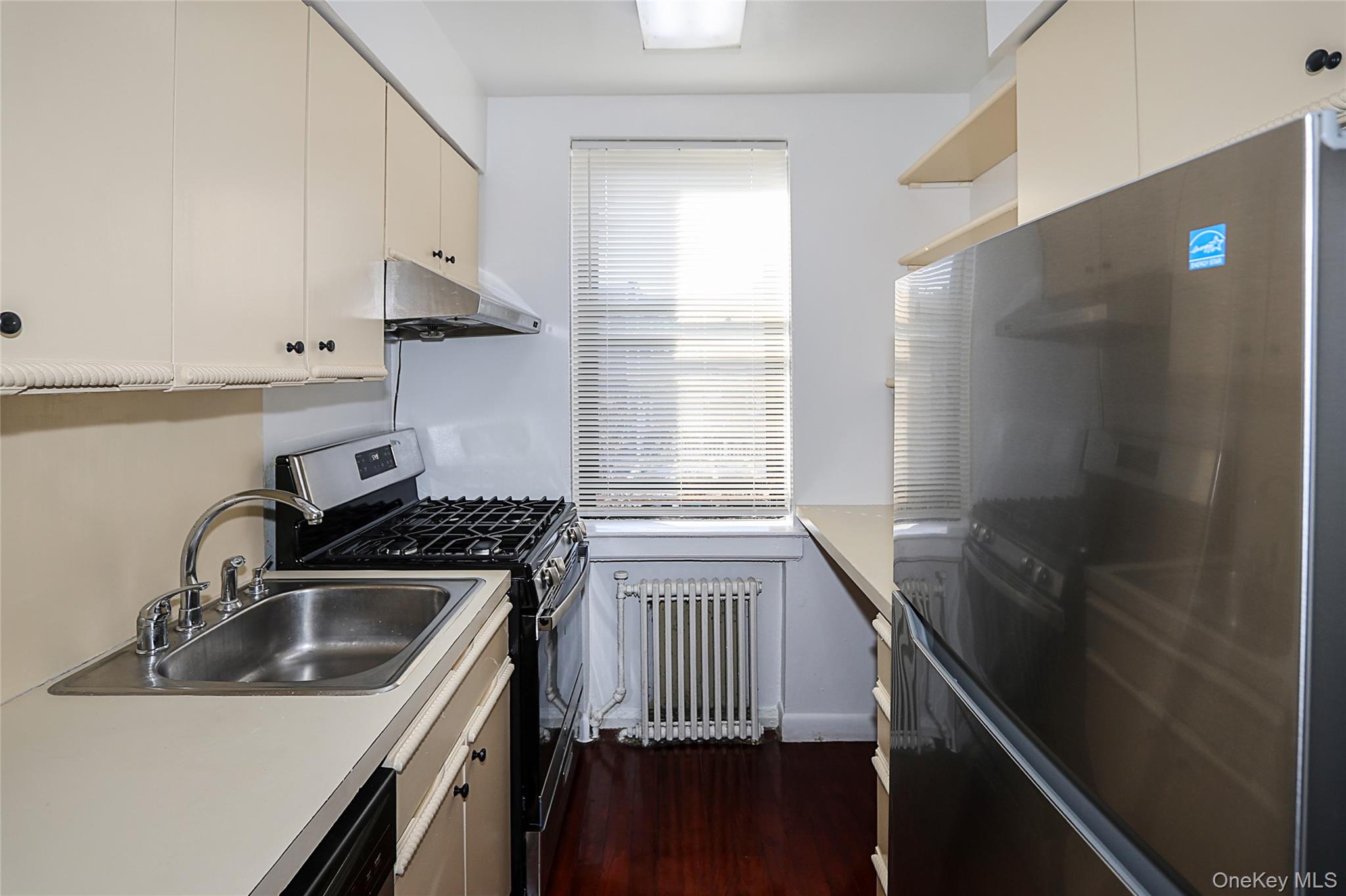47-22 215th Place, Unit 2C Queens, NY 11361 - Photo 15 of 26 Kitchen with stainless steel appliances, radiator heating unit, light countertops, under cabinet range hood, and open shelves
