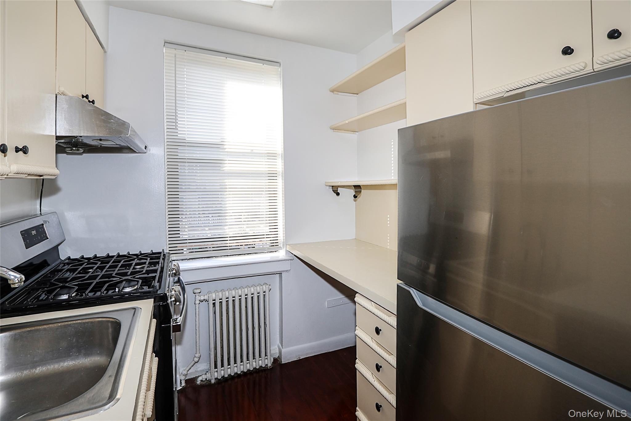 47-22 215th Place, Unit 2C Queens, NY 11361 - Photo 16 of 26 Kitchen featuring appliances with stainless steel finishes, open shelves, radiator heating unit, light countertops, and under cabinet range hood