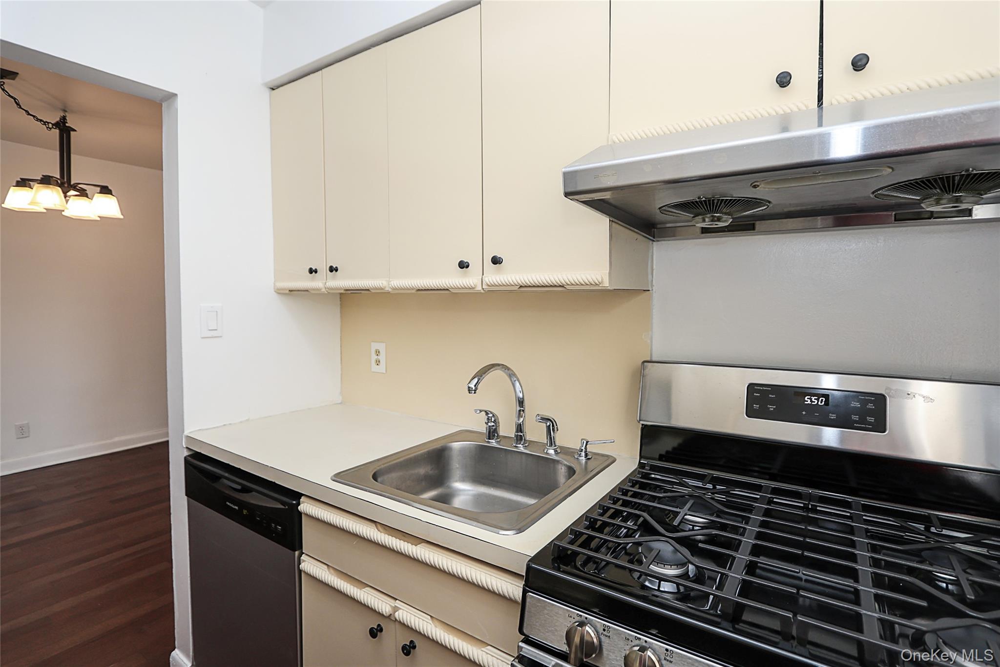 47-22 215th Place, Unit 2C Queens, NY 11361 - Photo 19 of 26 Kitchen featuring appliances with stainless steel finishes, light countertops, under cabinet range hood, decorative light fixtures, and dark wood-type flooring