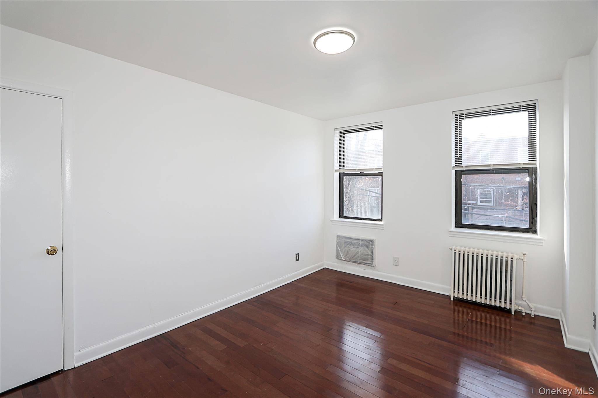 47-22 215th Place, Unit 2C Queens, NY 11361 - Photo 20 of 26 Empty room featuring radiator and dark wood-type flooring