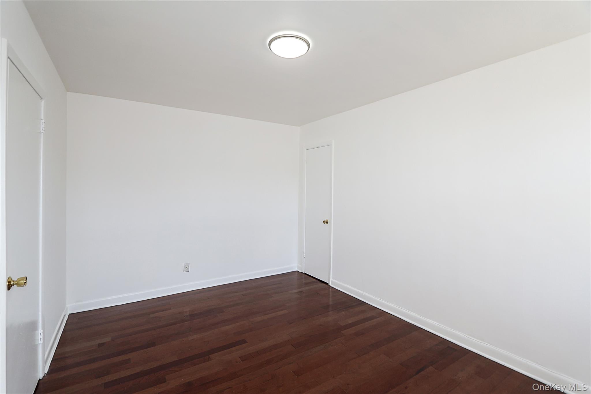 47-22 215th Place, Unit 2C Queens, NY 11361 - Photo 21 of 26 Empty room featuring dark wood-style floors and baseboards