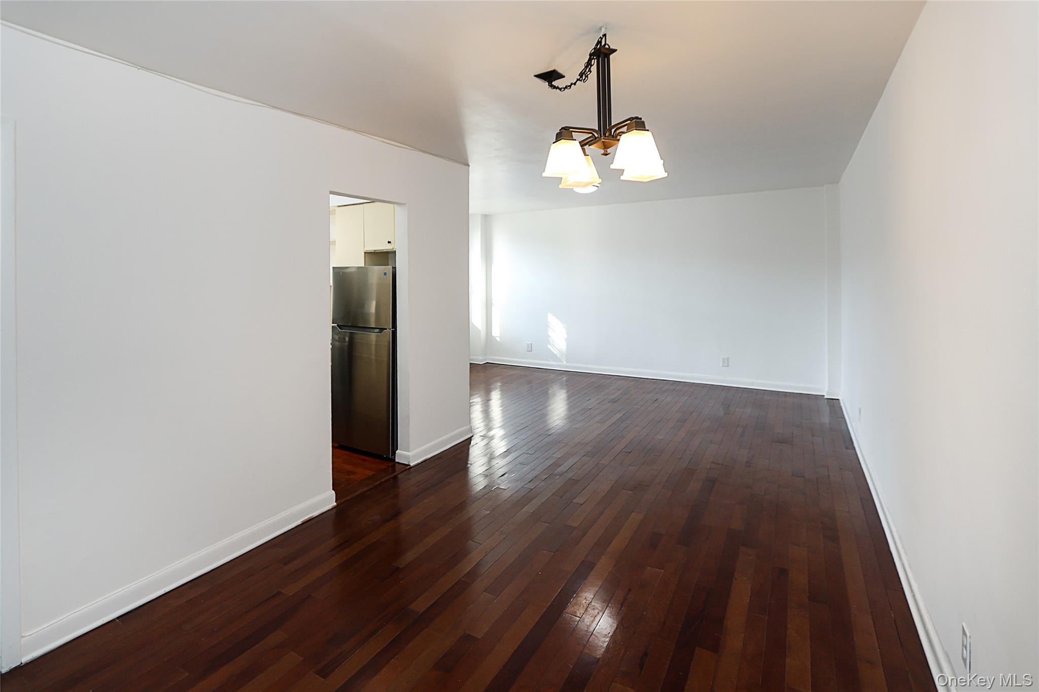 47-22 215th Place, Unit 2C Queens, NY 11361 - Photo 4 of 26 Empty room with a chandelier and dark wood-style flooring