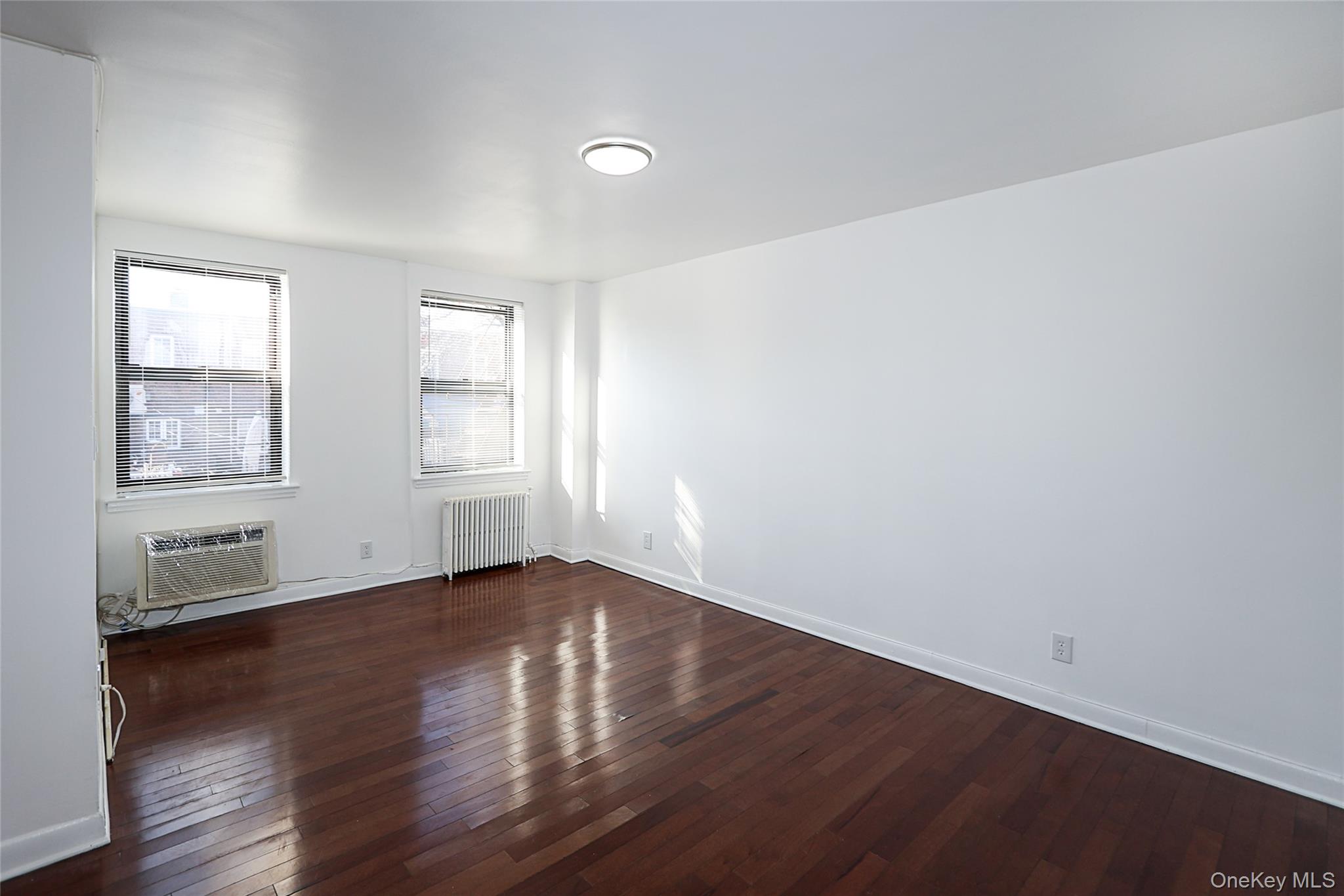 47-22 215th Place, Unit 2C Queens, NY 11361 - Photo 10 of 26 Spare room with radiator heating unit and dark wood-style flooring