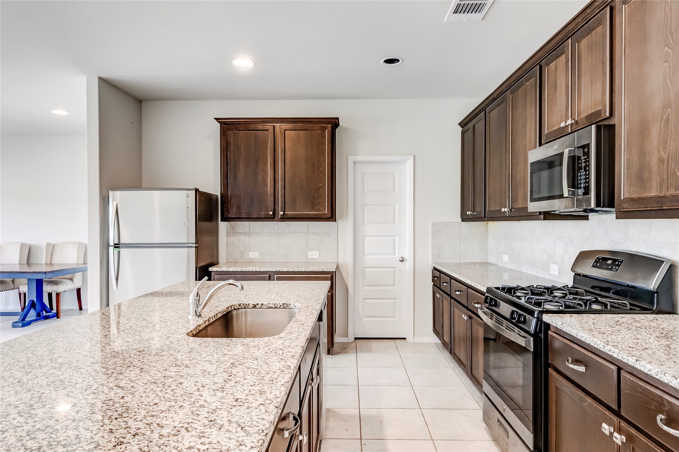 2721 Winding Creek Road Kyle, TX 78640 - Photo 11 of 27 Kitchen featuring a large central island with an undermount sink, granite countertops, dark wood cabinetry, stainless steel appliances, and a tile backsplash