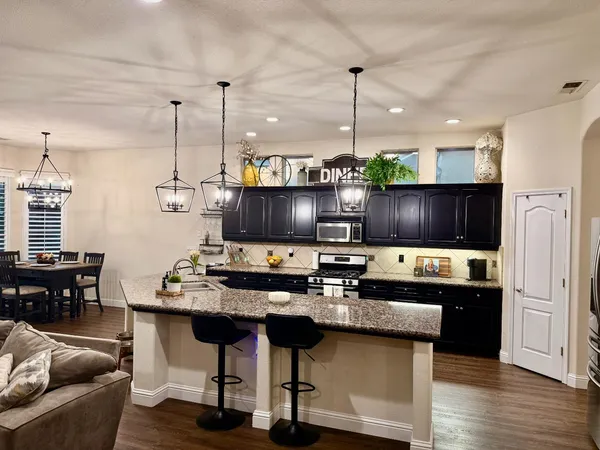 a kitchen with stainless steel appliances granite countertop a stove top oven a refrigerator a kitchen island a dining table and chairs with wooden floor