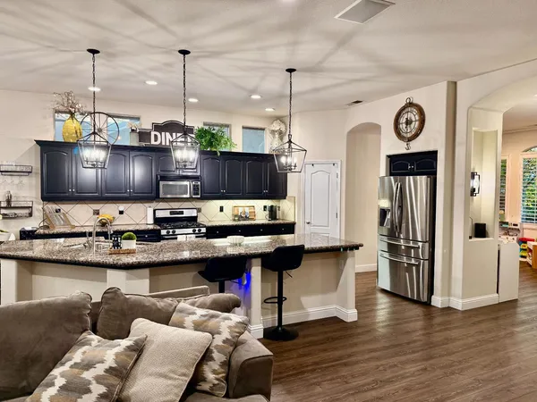 a kitchen with stainless steel appliances granite countertop a sink dishwasher and a refrigerator with wooden floor