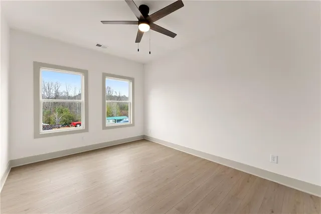 an empty room with wooden floor chandelier fan and windows