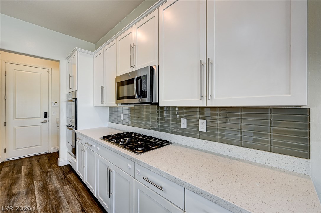 8197 Riley Love Street Las Vegas, NV 89139 - Photo 19 of 48 A well-appointed kitchen features white cabinetry, stone countertops, and dark wood flooring.