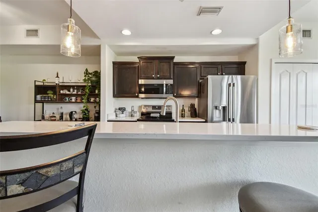 a kitchen with stainless steel appliances a sink a stove a refrigerator cabinets and a dining table with wooden floor