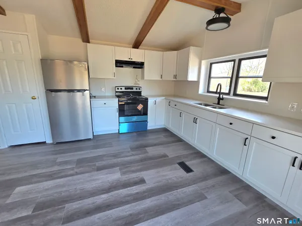 a kitchen with granite countertop a refrigerator a sink dishwasher a stove and white cabinets with wooden floor