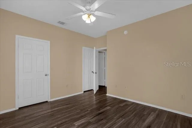 a view of an empty room with wooden floor and a ceiling fan
