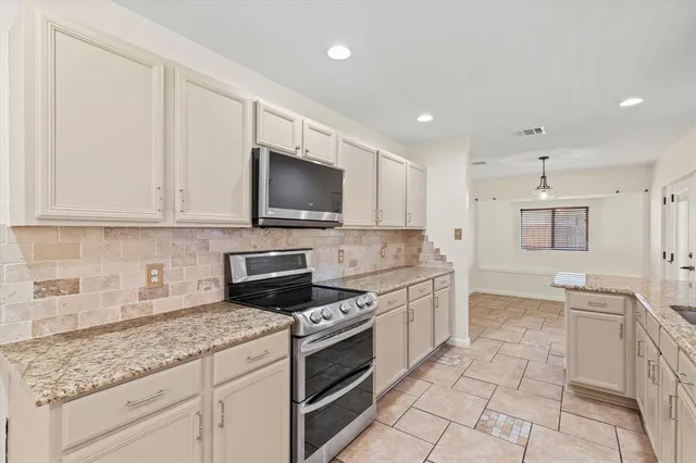 a kitchen with granite countertop a sink a stove top oven and cabinetry