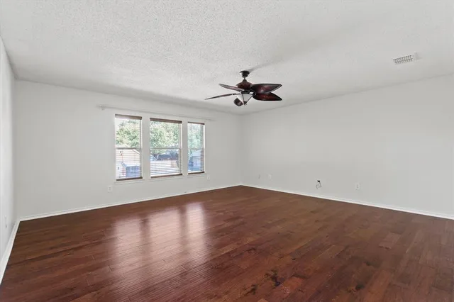an empty room with wooden floor fan and windows