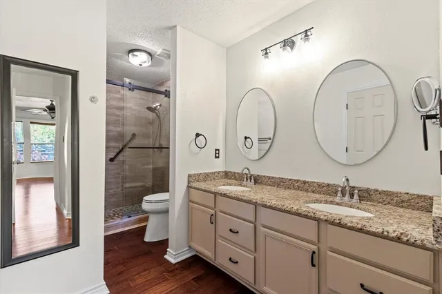 a bathroom with a granite countertop toilet a double vanity sink and a mirror