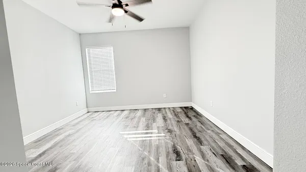 an empty room with wooden floor fan and windows