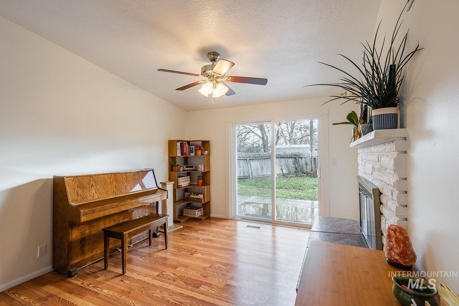 6403 Colonial Drive Boise, ID 83709 - Photo 11 of 42 Sitting room featuring light wood-style flooring, a stone fireplace, a textured ceiling, and a ceiling fan