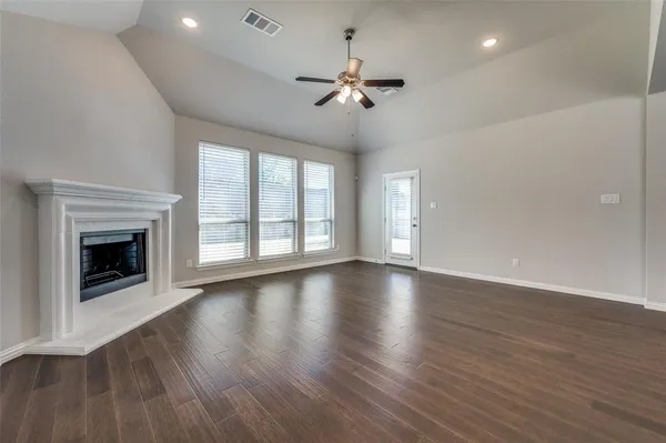 a view of an empty room with wooden floor fireplace and a window