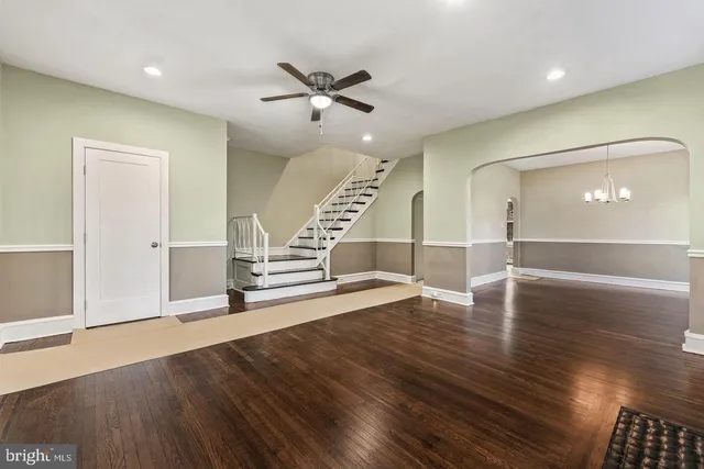 a view of an empty room with wooden floor stairs and a chandelier