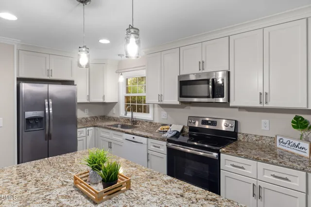 a kitchen with granite countertop a stove a sink a microwave a refrigerator and cabinets