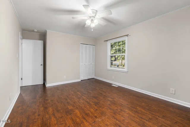 an empty room with wooden floor chandelier fan and windows