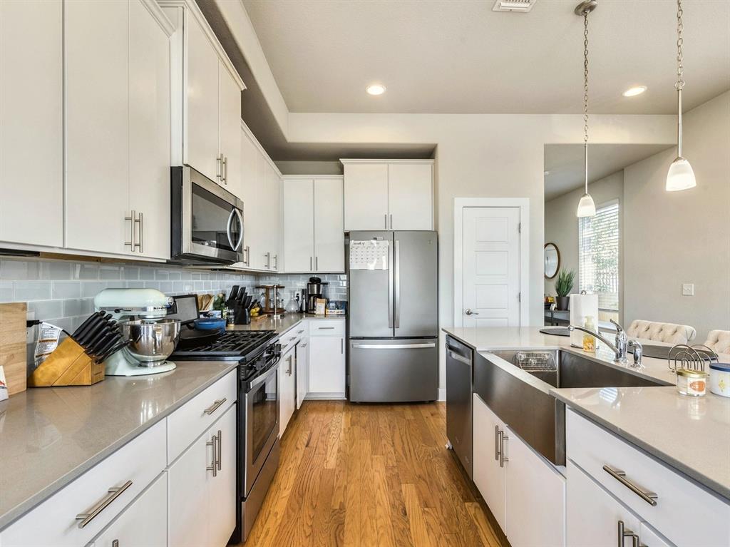 7001 Brick Slope Path Austin, TX 78744 - Photo 7 of 27 Kitchen with white cabinets, stainless steel appliances, light wood-style flooring, backsplash, and decorative light fixtures