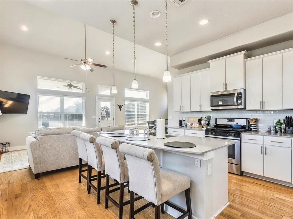 7001 Brick Slope Path Austin, TX 78744 - Photo 8 of 27 Kitchen featuring tasteful backsplash, a center island with sink, appliances with stainless steel finishes, a kitchen breakfast bar, and white cabinetry