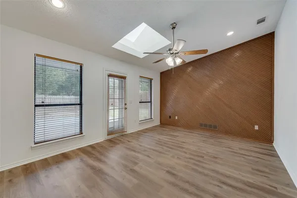 an empty room with wooden floor fan and windows